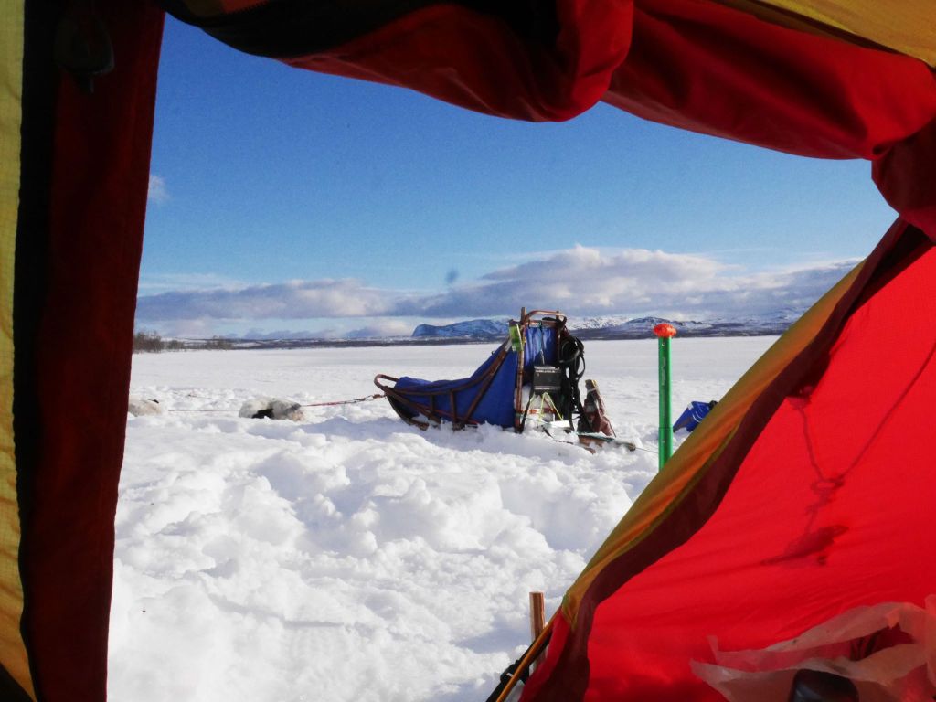 View from a tent of a snowy landscape with a sled and hills in the background.