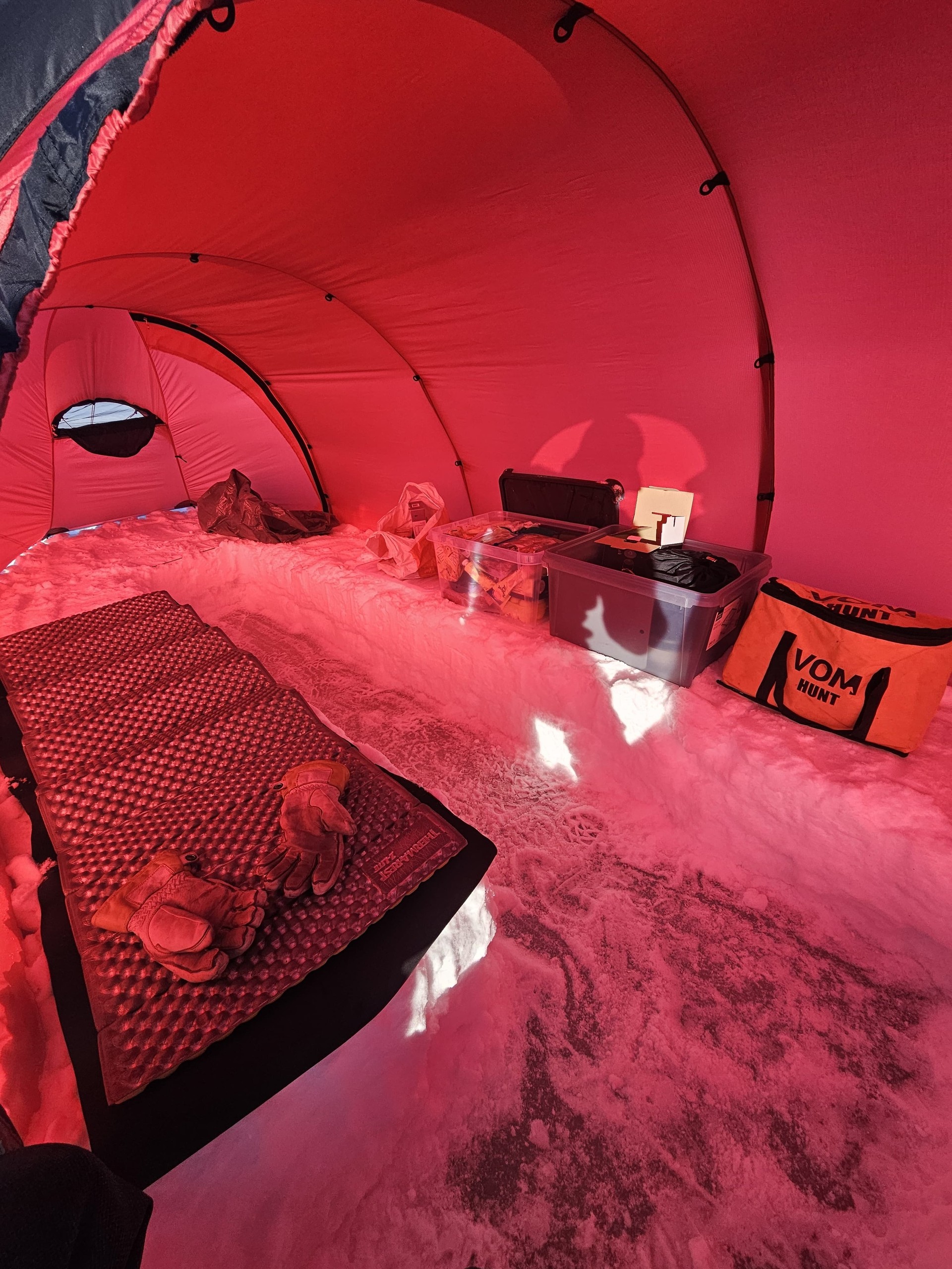 Inside view of a red tent on snow with gear, sleeping pad, and gloves.