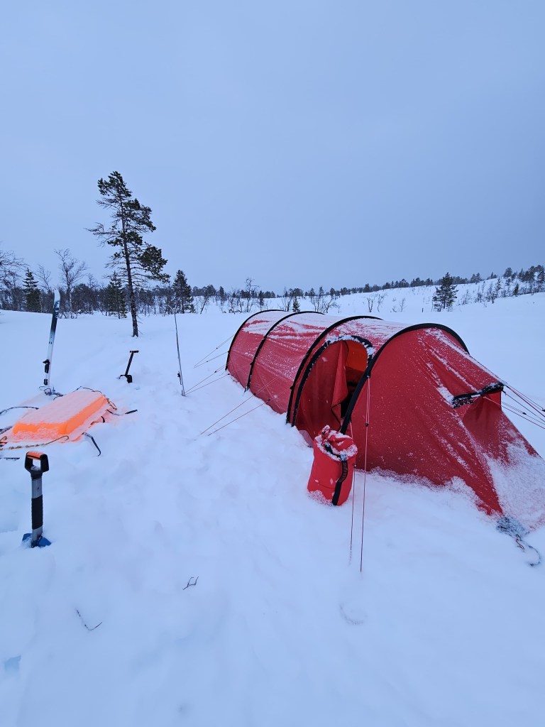 Red tent in snowy landscape with trees and equipment nearby.