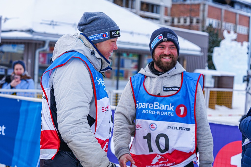 Two smiling men in winter gear at a snowy outdoor event.