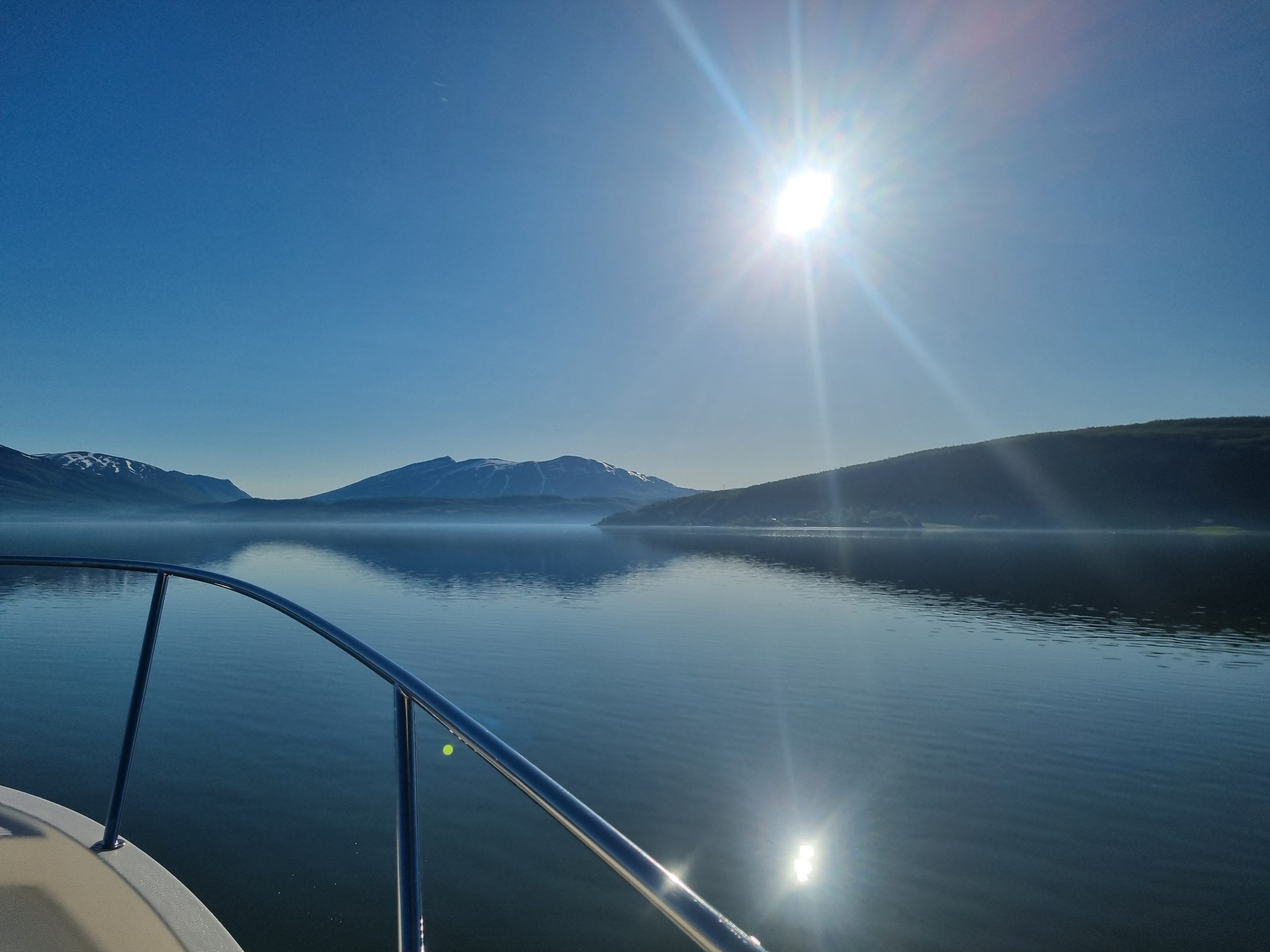 Sunlit mountain lake view from boat, clear sky and calm water.