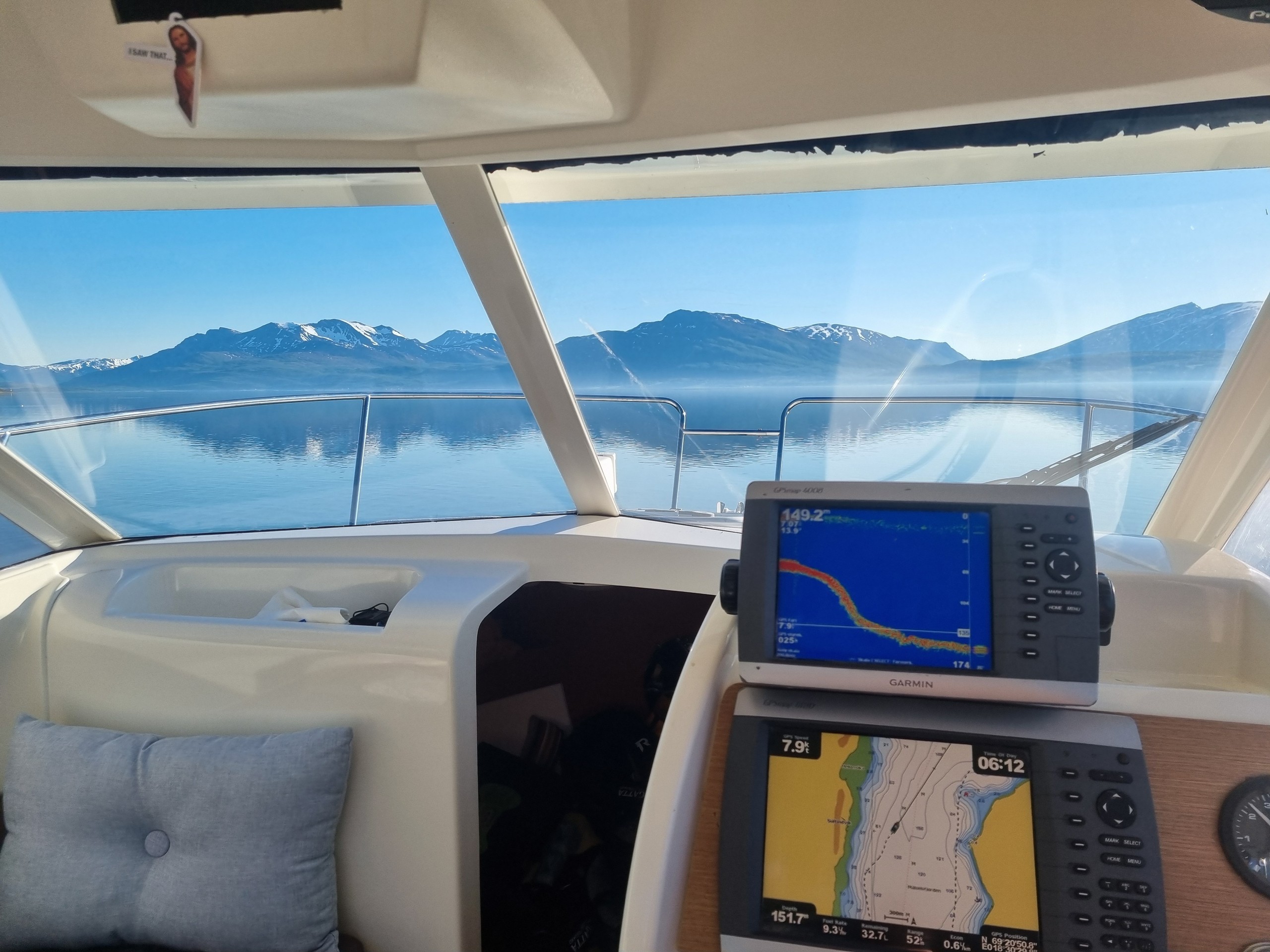 Boat cabin with navigation screens, mountains and calm water view outside.