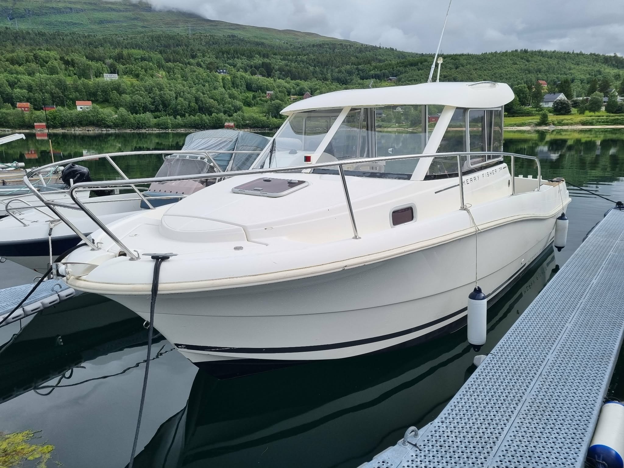 White boat docked on calm water, surrounded by greenery.