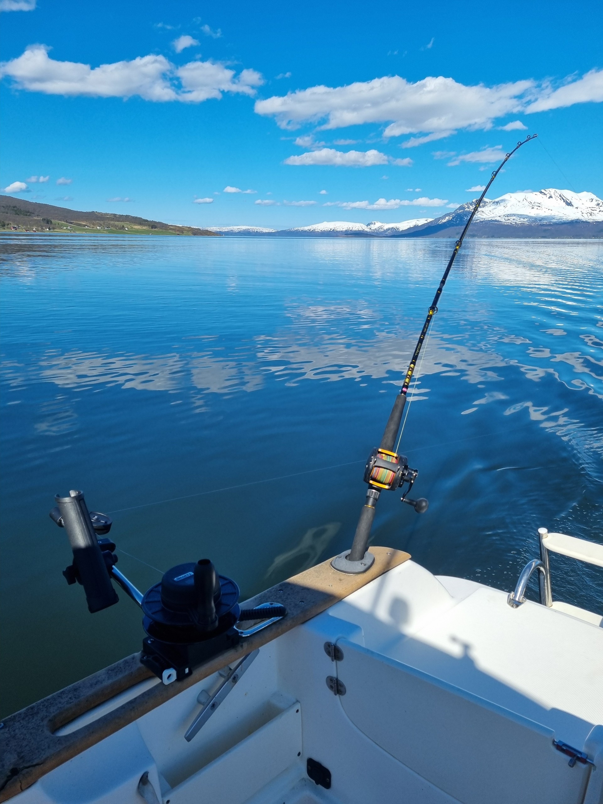 Fishing rod on boat with snowy mountains and calm blue lake view.