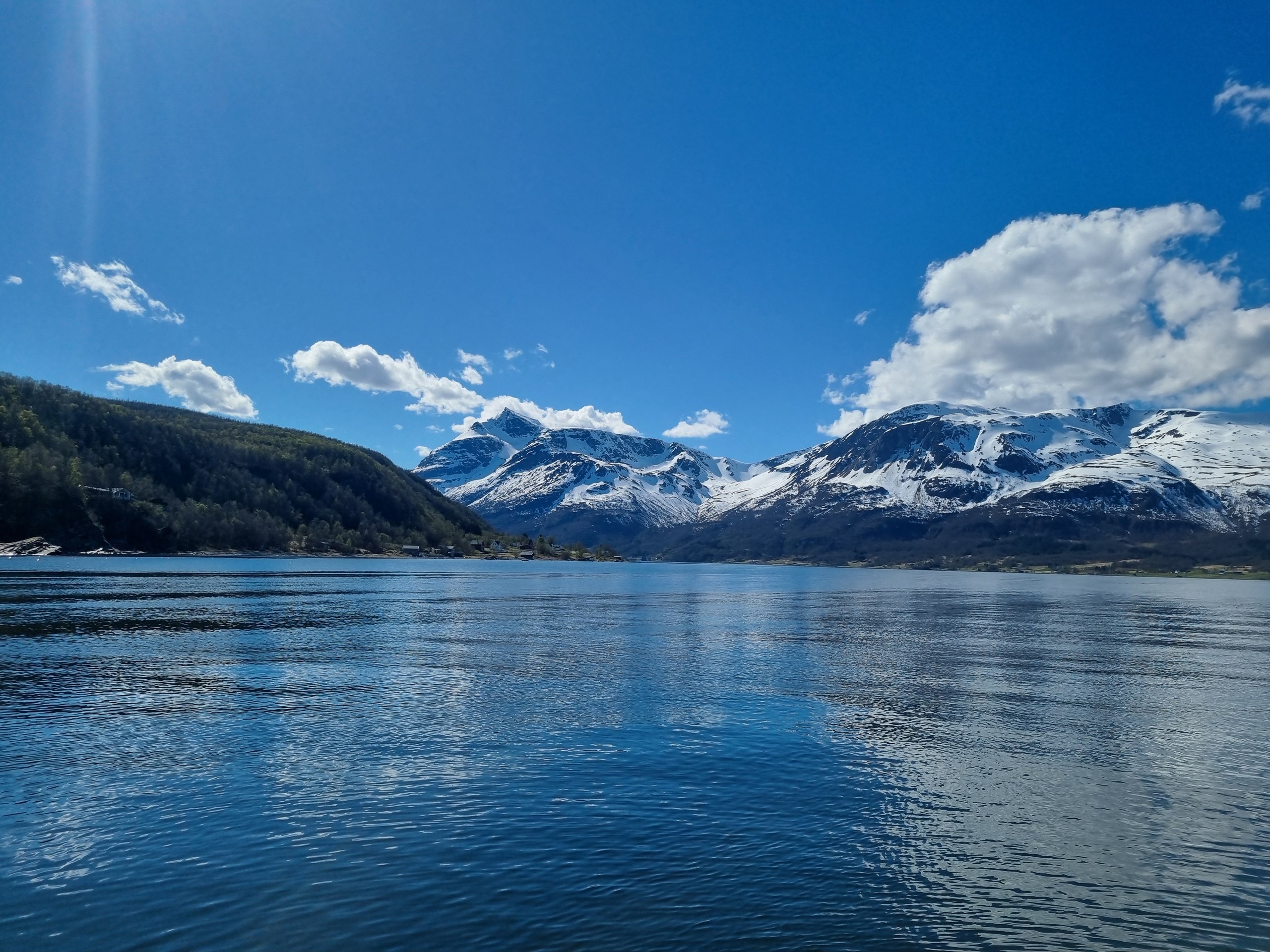 Snow-capped mountains and clear lake under a blue sky with clouds.