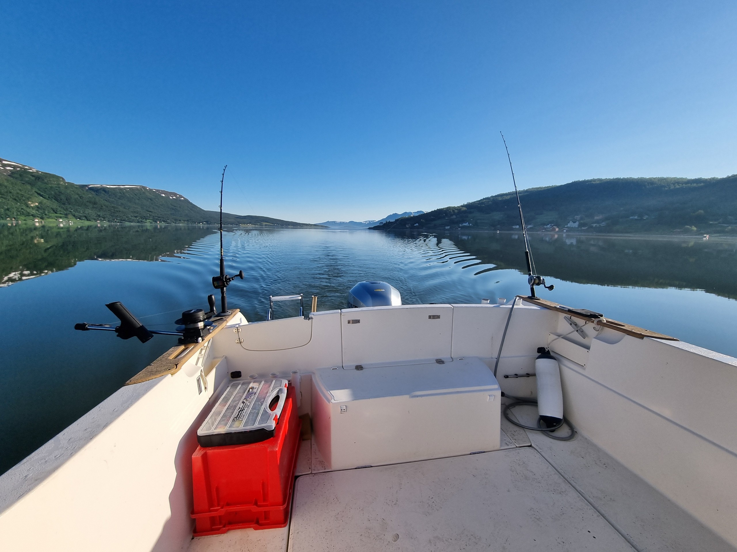 View from a boat with fishing rods, calm lake, and mountains in the background.