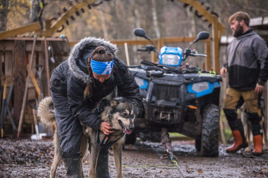 Person tending to a dog near an ATV; another person stands nearby.