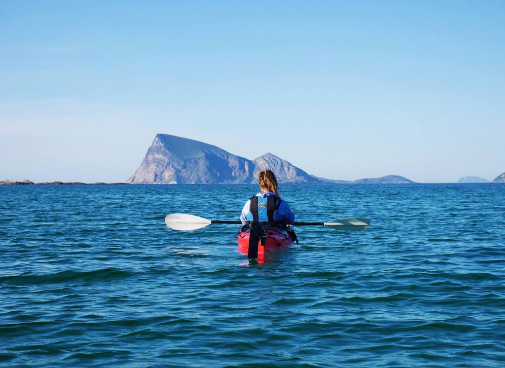 Person kayaking on calm sea towards distant island under clear sky.