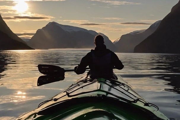 Person kayaking on a calm lake surrounded by mountains at sunset.
